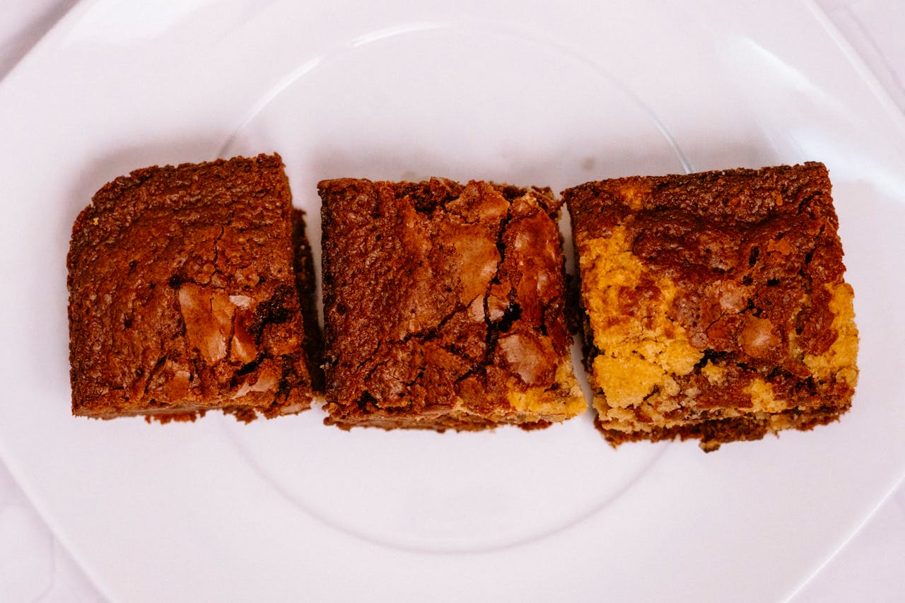 about-us-02 Three decadent brownie squares on a white plate, showcasing rich textures and flavors.